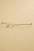 Brass-colored towel bar with a wavy organic shape, shown in a studio setting on a neutral background.