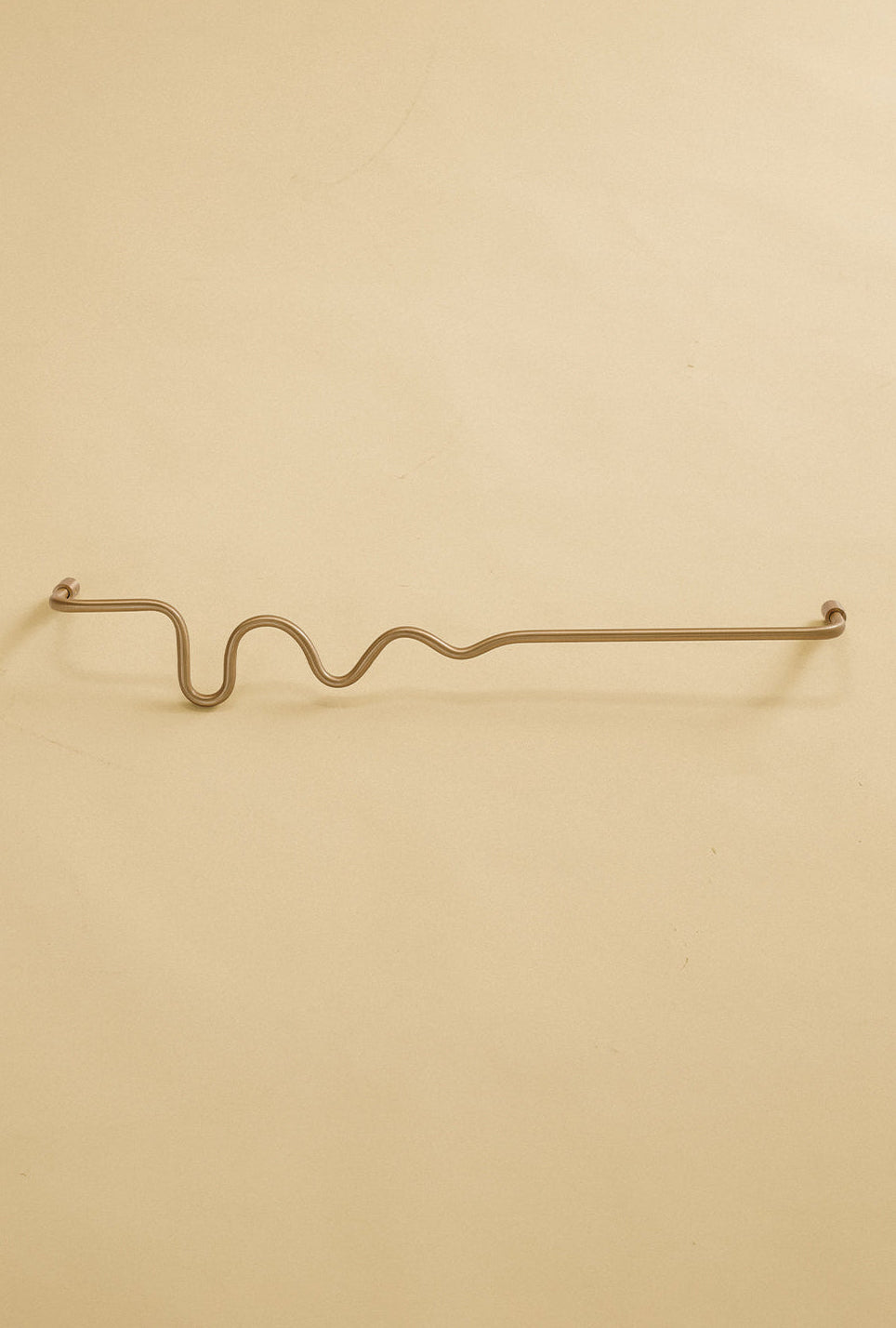 Brass-colored towel bar with a wavy organic shape, shown in a studio setting on a neutral background.