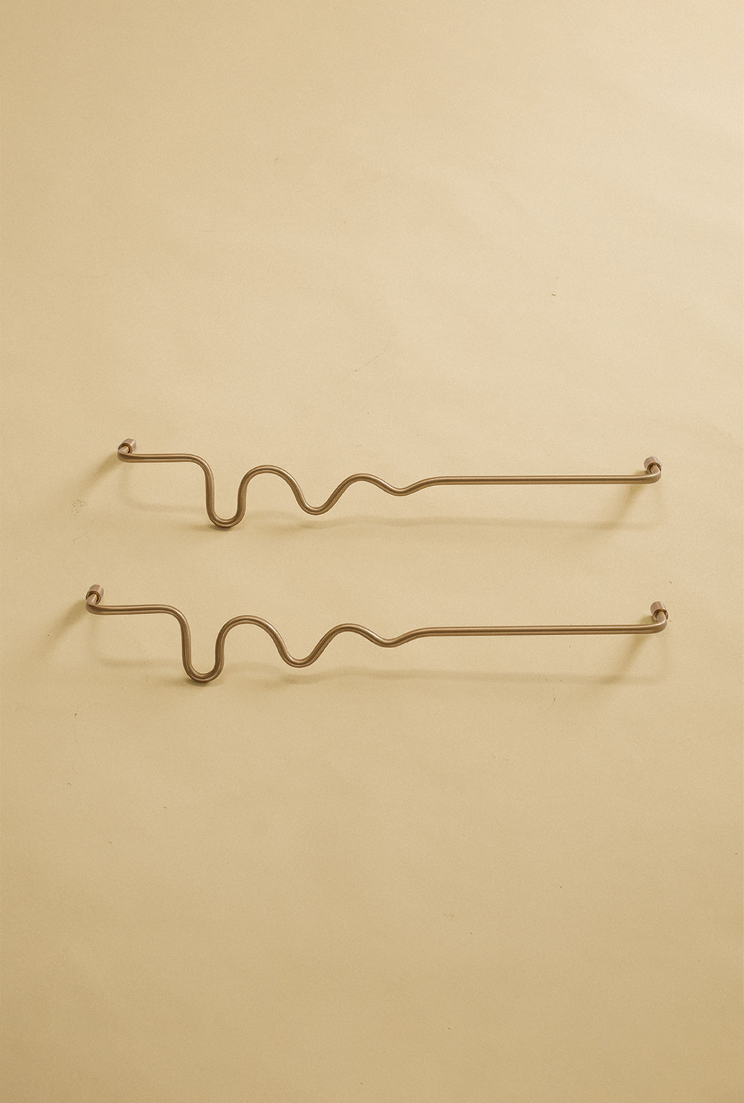 Two brass wavy towel bars displayed on a neutral studio background.