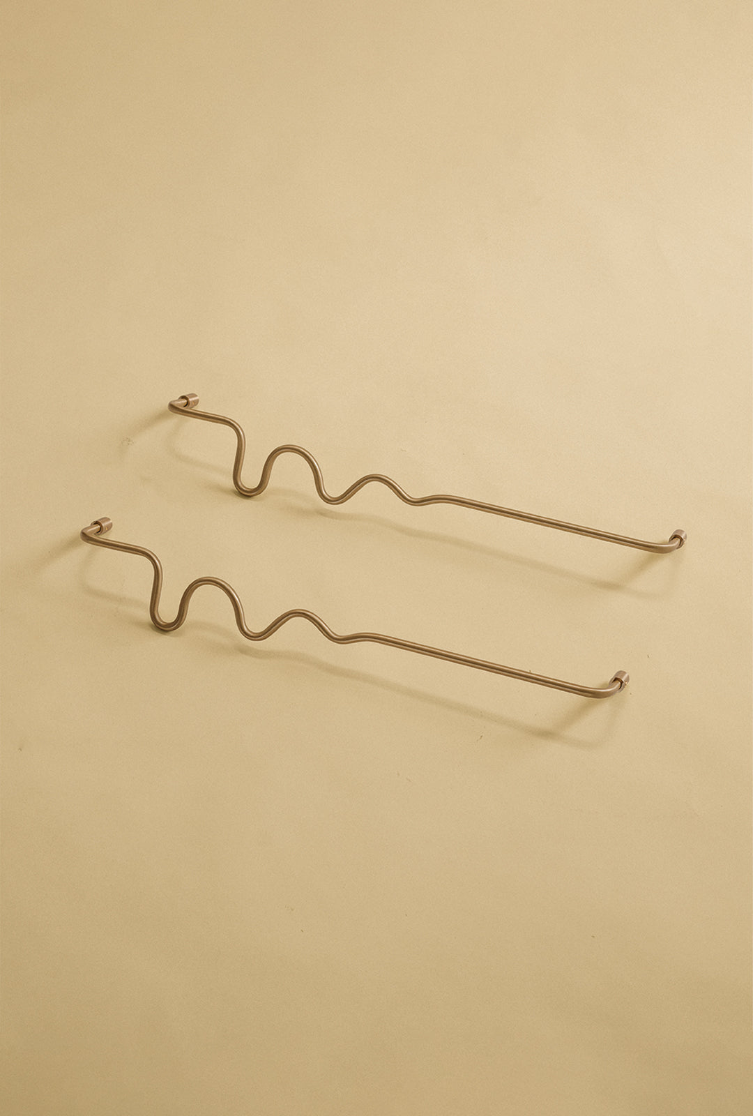 Two brass wavy towel bars displayed on a neutral studio background.
