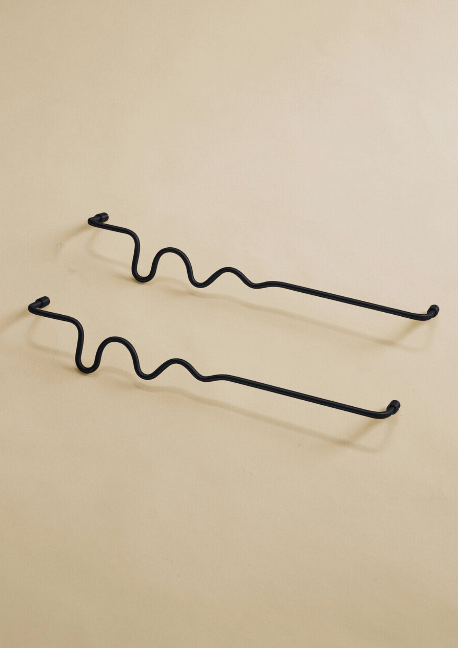 Two black wavy towel bars displayed on a neutral studio background.