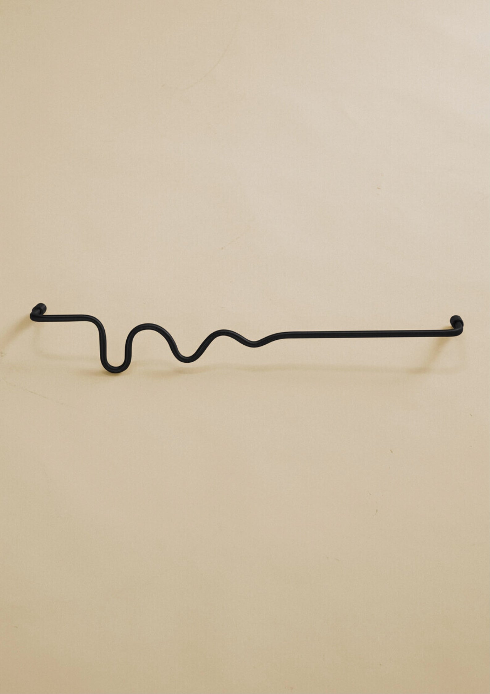 Black-colored towel bar with a wavy organic shape, shown in a studio setting on a neutral background.