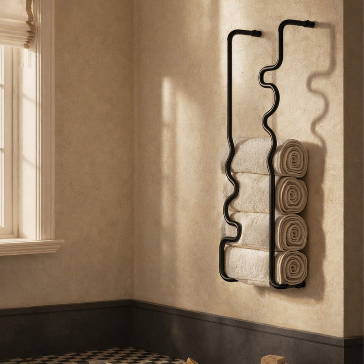 Two black wavy brass towel bars mounted in a bathroom, holding neatly rolled towels beside a bathtub in natural light.
