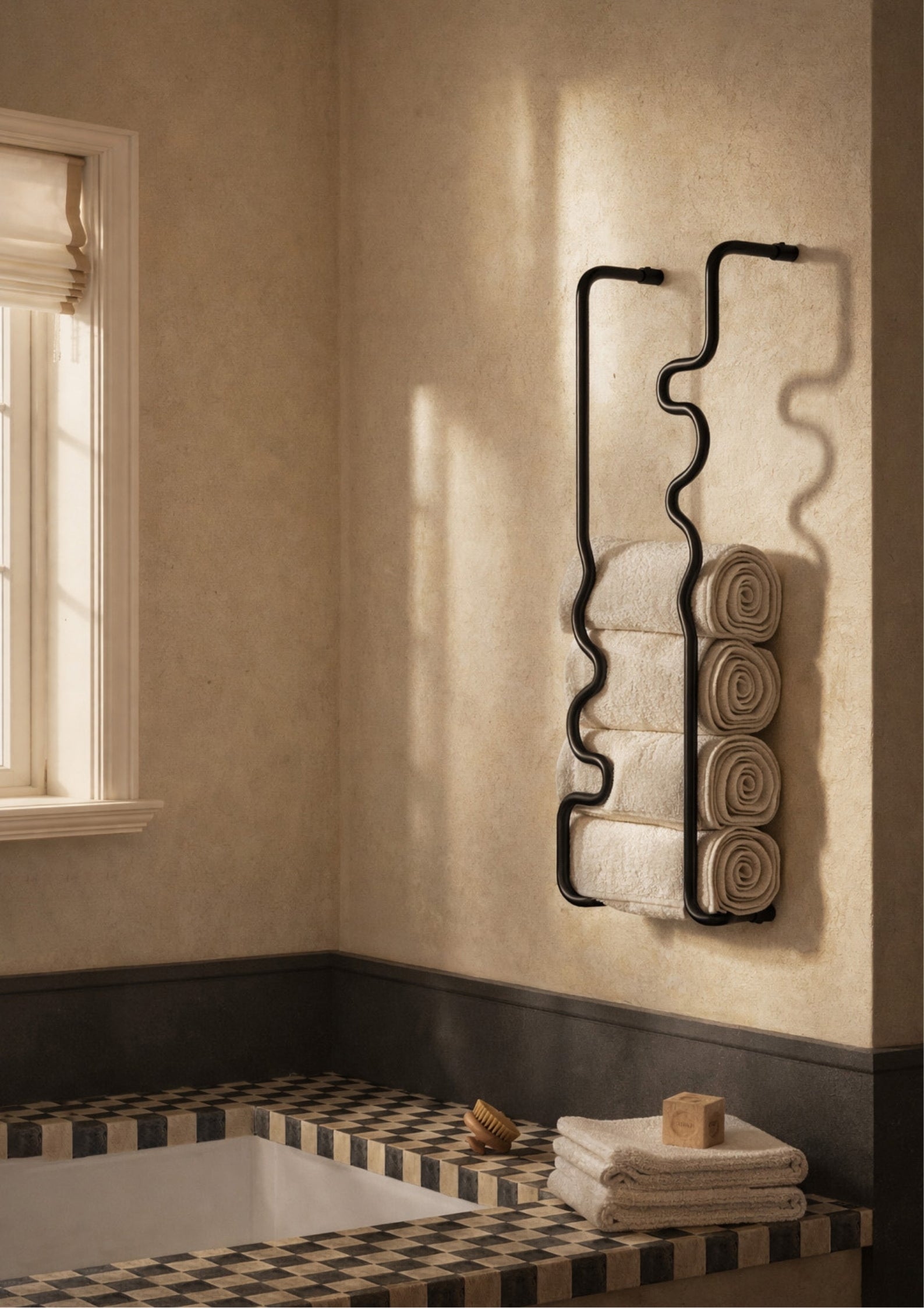 Two black wavy brass towel bars mounted in a bathroom, holding neatly rolled towels beside a bathtub in natural light.