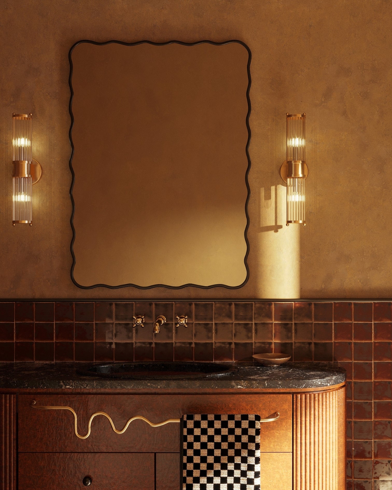 Wavy-edged mirror above a bathroom sink with wall lights and a towel hanging from a curved brass towel bar.