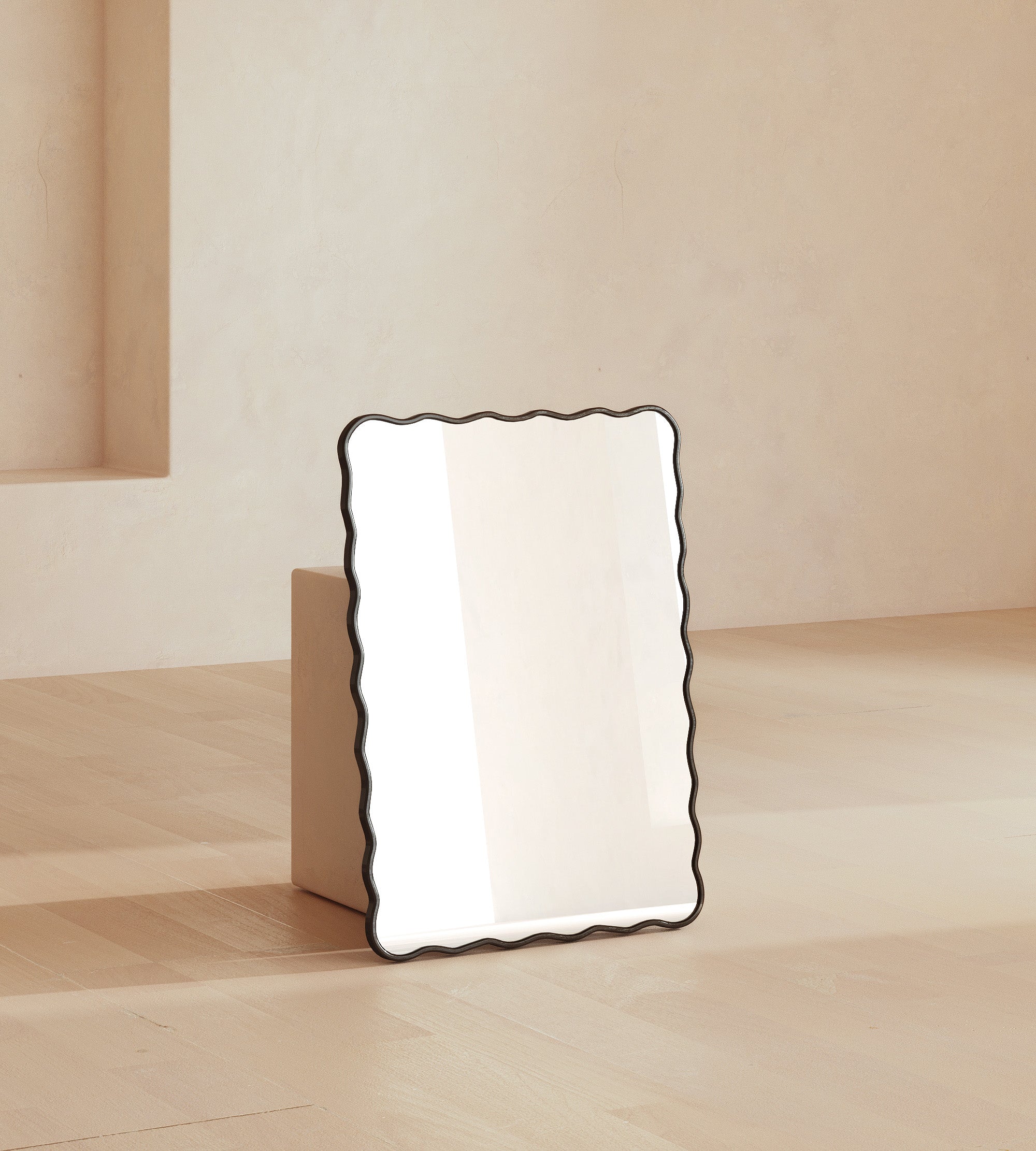 Rectangular wall mirror with a black frame and softly wavy edges, leaning against a wall in a neutral interior setting.
