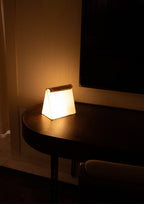 Small glowing table lamp on a round wooden side table.