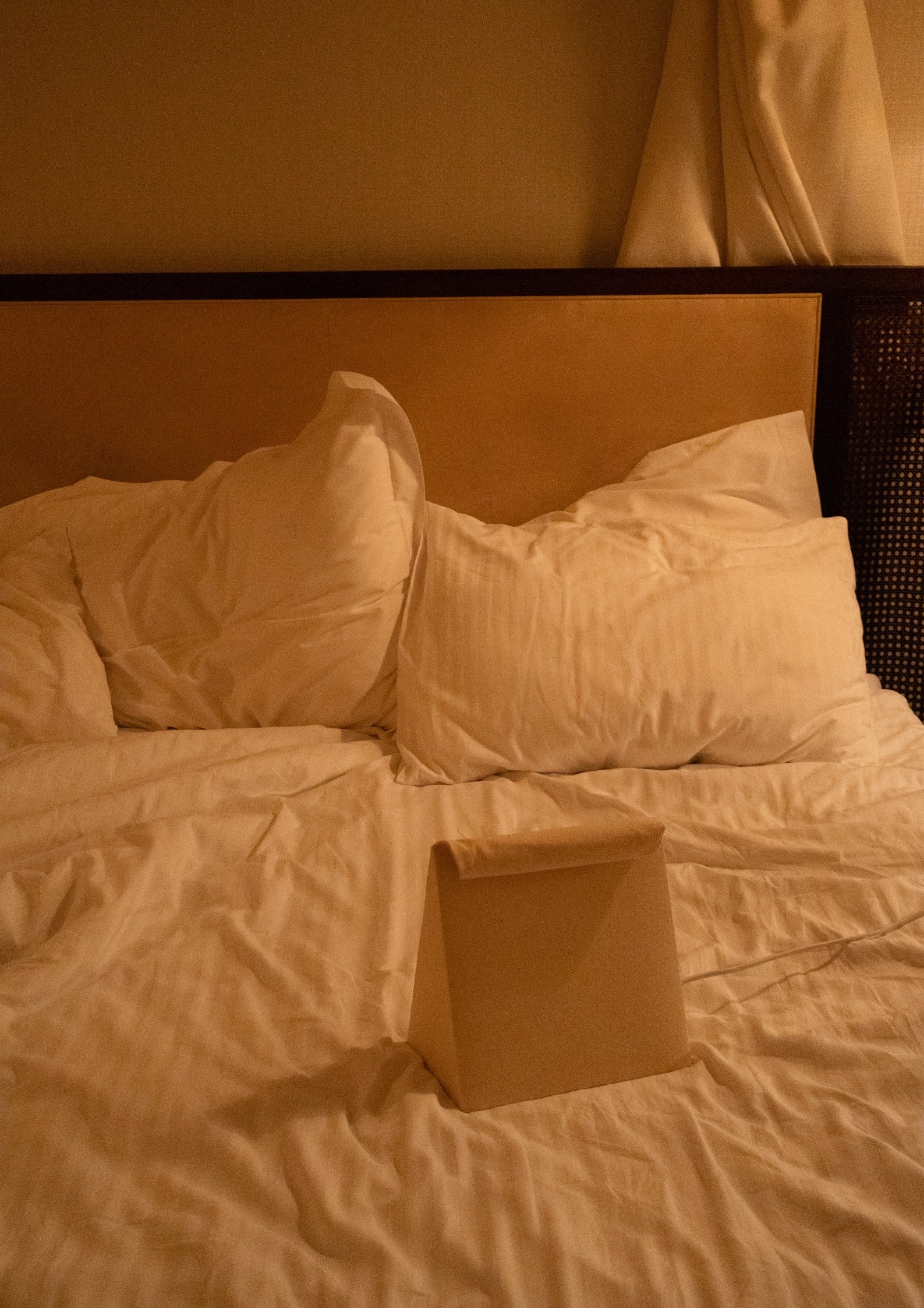 Small fabric lamp resting on a bed with white pillows and sheets.