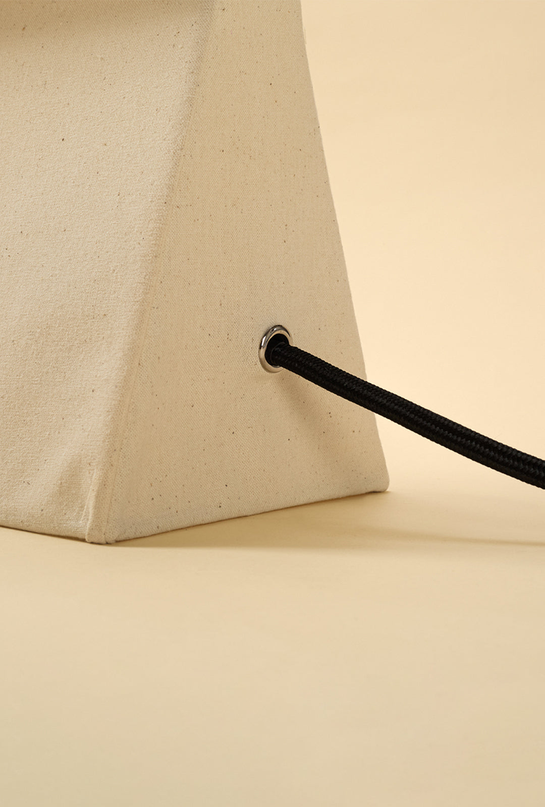 Close-up detail of a linen table lamp showing the textured fabric surface and black braided power cord.