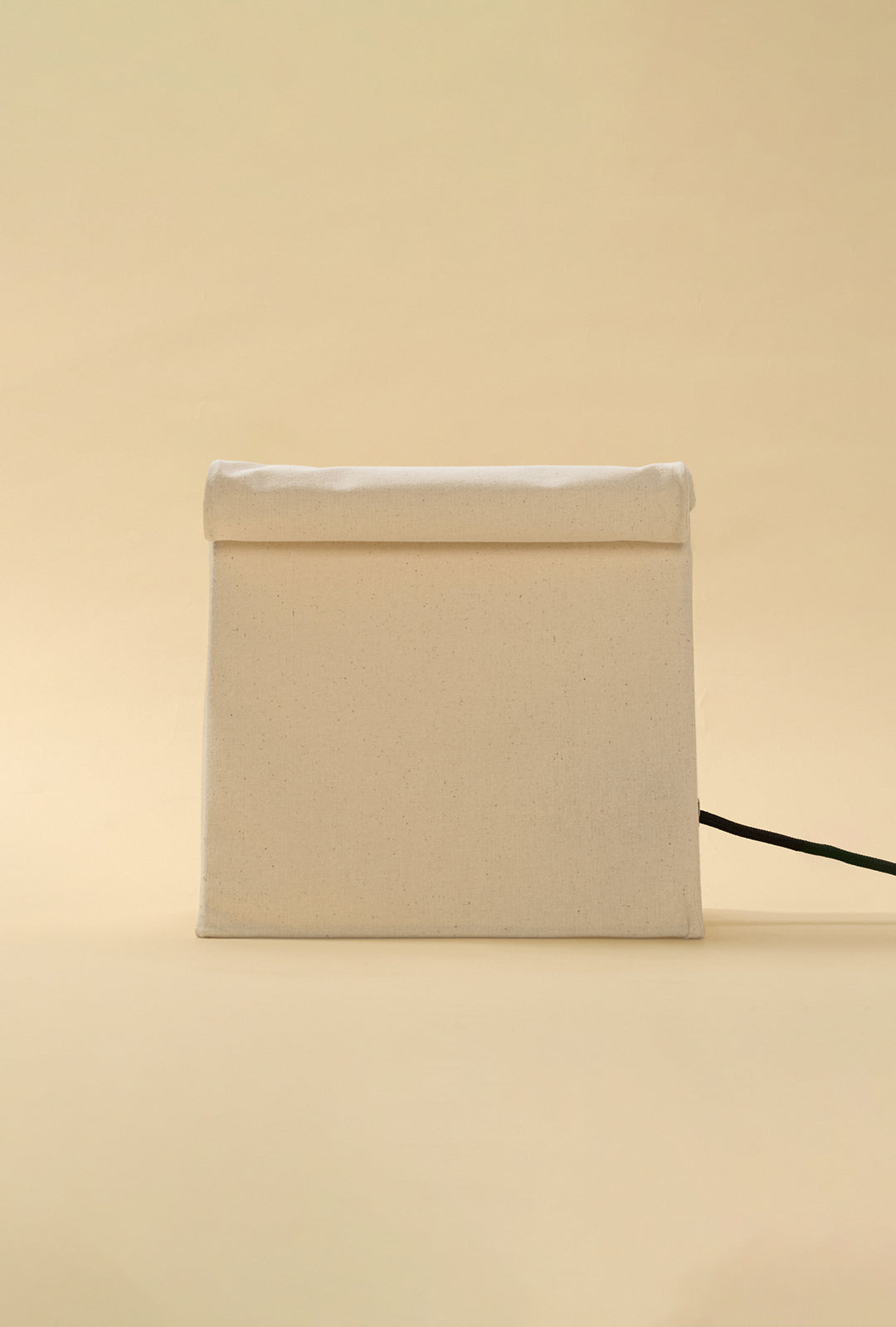 Front view of an unlit linen table lamp with a rolled top design.