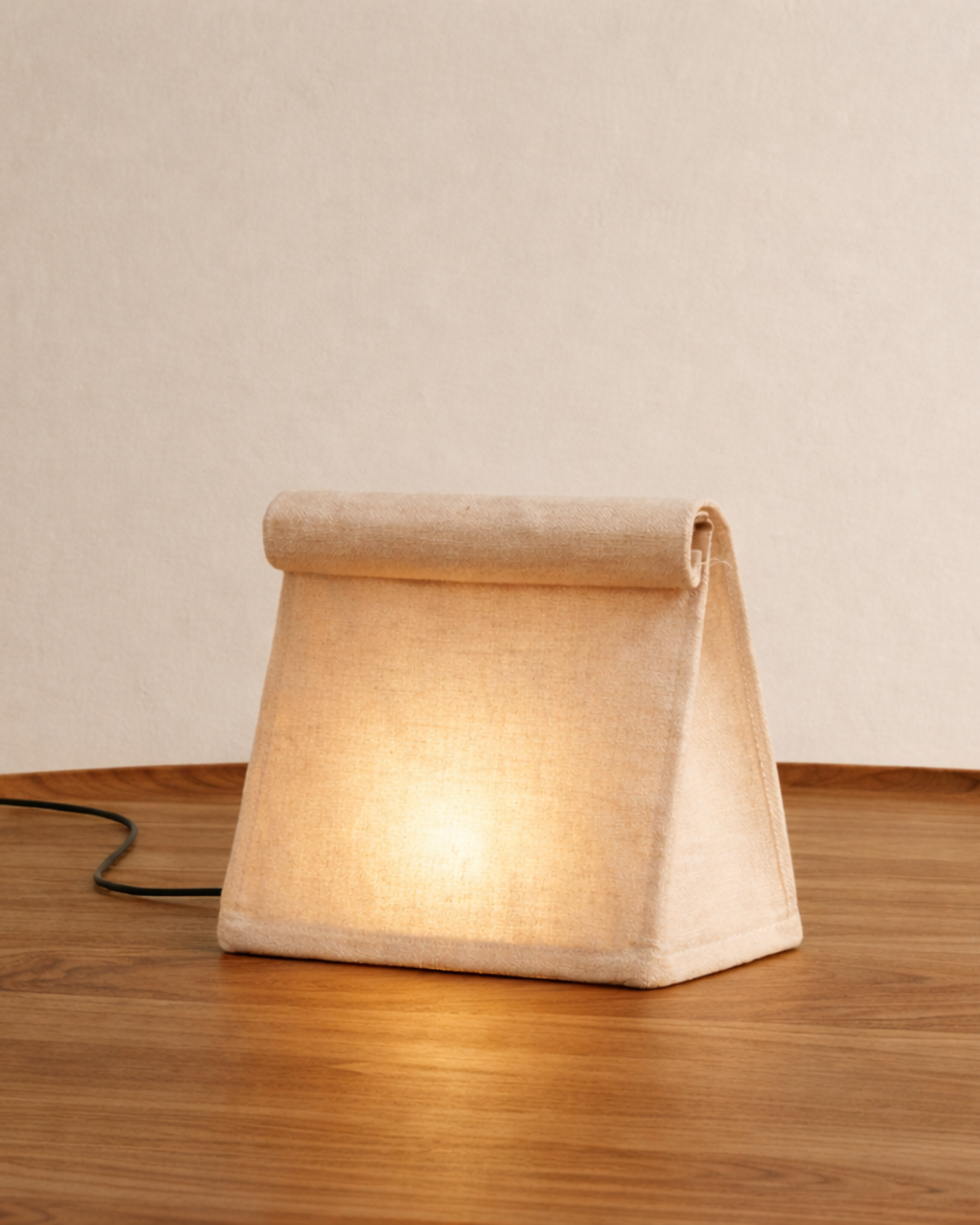 Fabric table lamp with a soft warm glow on a wooden surface.
