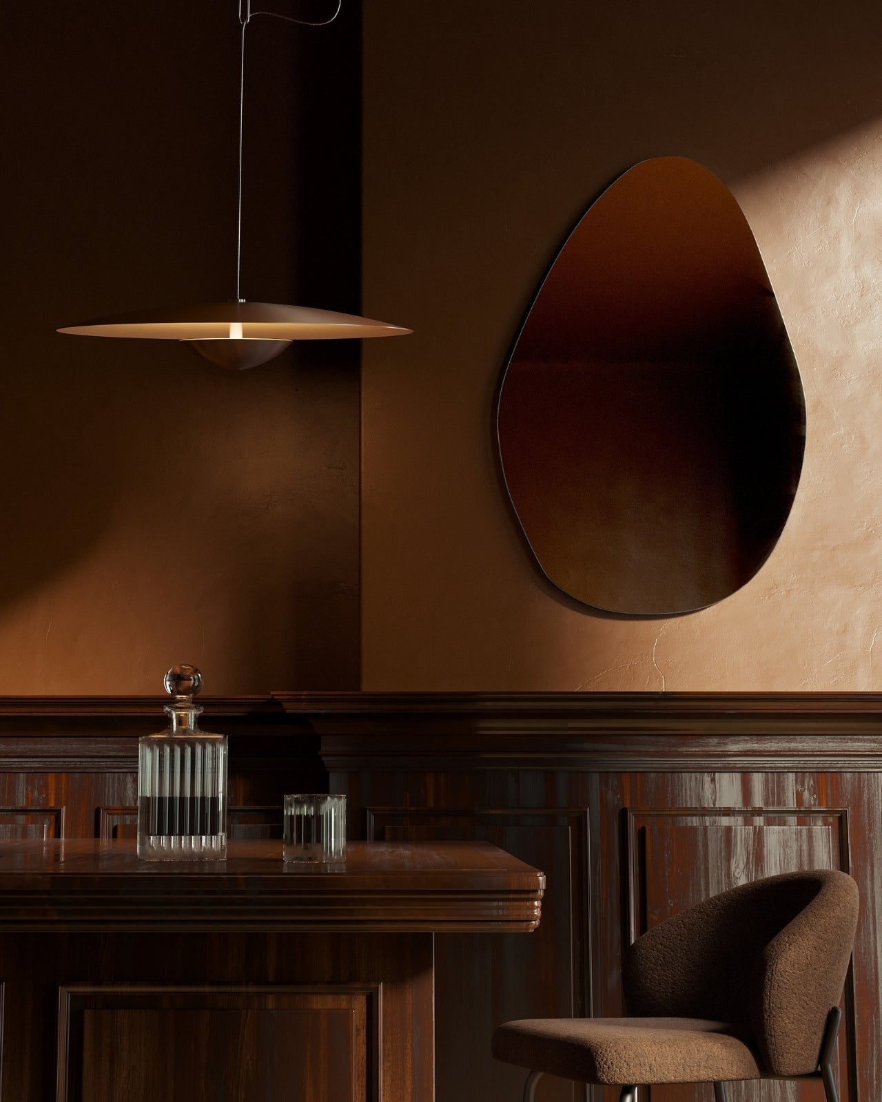 Pebble-shaped frameless wall mirror mounted above a wooden desk in a dimly lit interior.