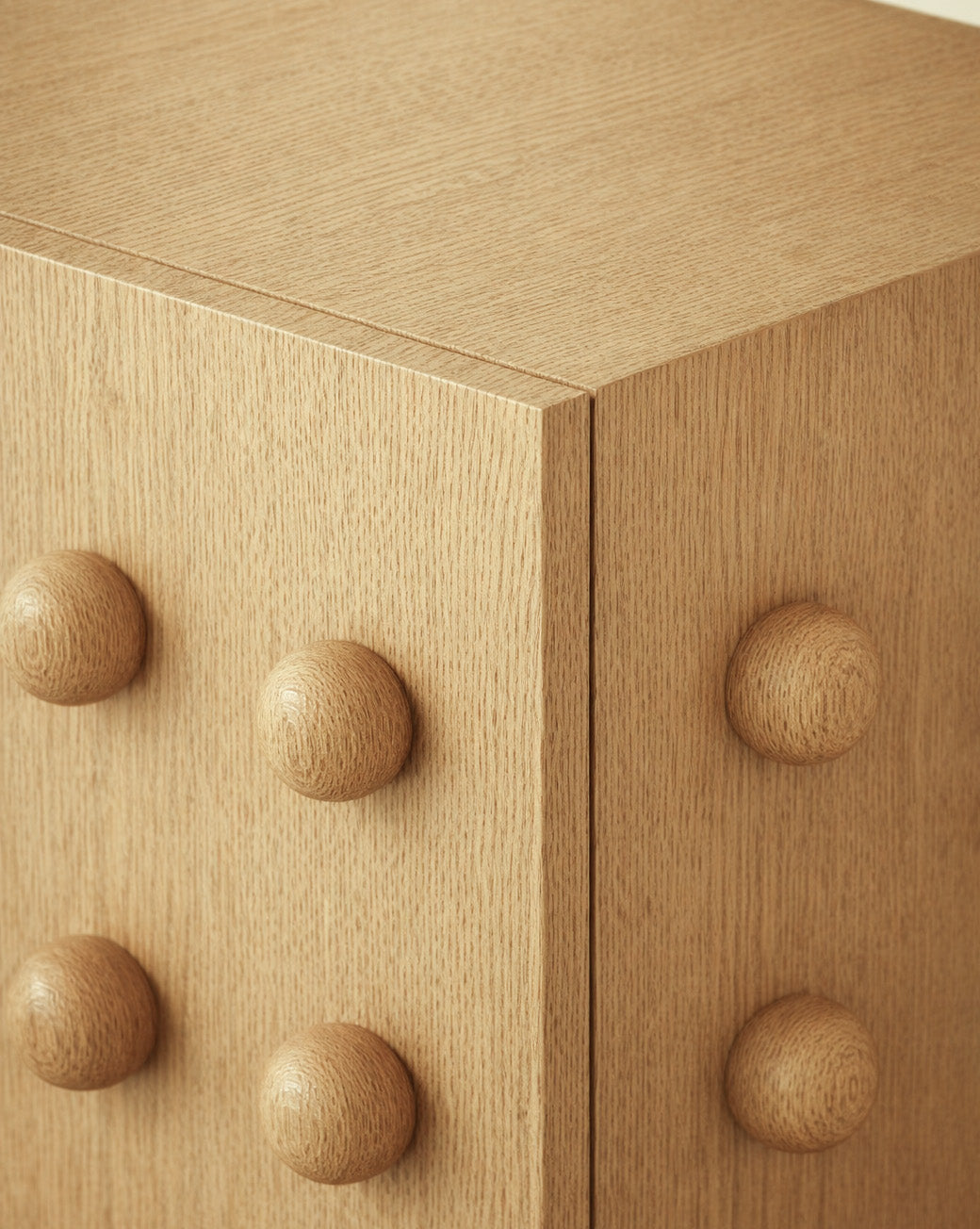 Close-up of a wooden storage cabinet showing a sculptural front with evenly spaced rounded wooden spheres and a smooth wood grain finish.