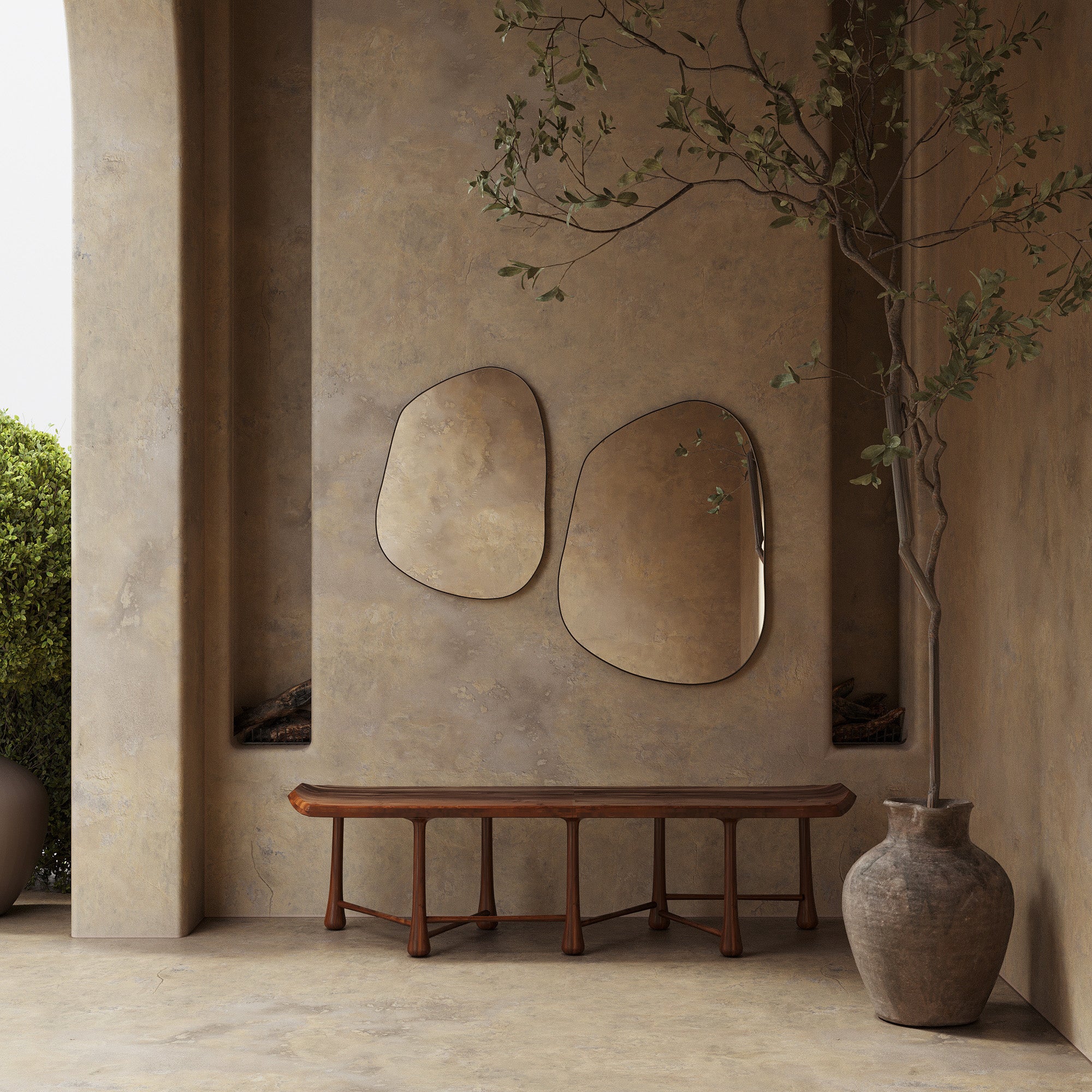 A wooden bench placed against a textured wall, with two irregularly shaped wall mirrors above it and a tall potted tree positioned to the right.