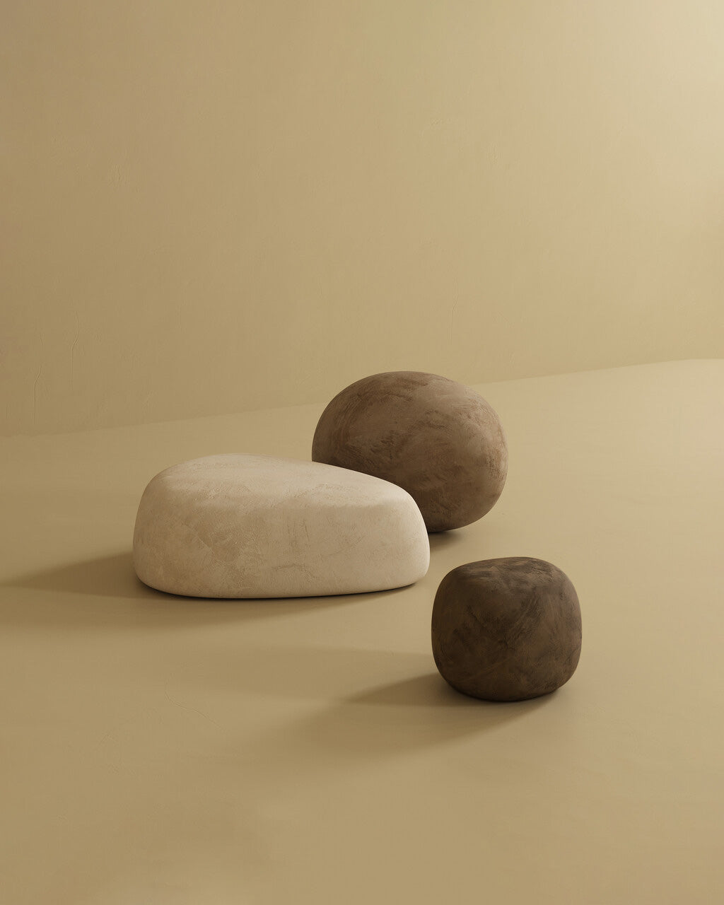 Three pebble-shaped ottomans in neutral tones, including one large off-white ottoman and two smaller brown ottomans, arranged on a minimalist beige studio background.