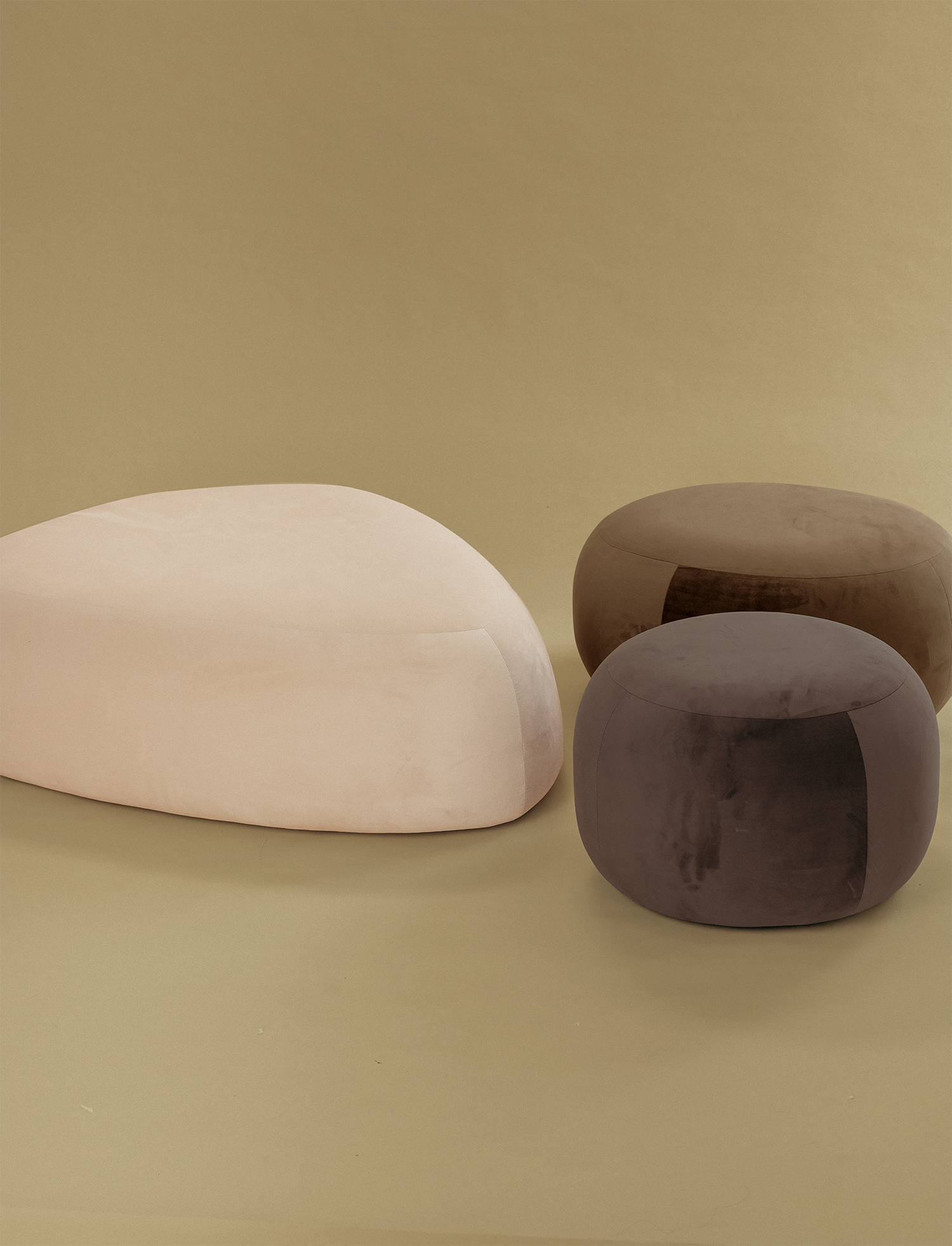 Pebble-shaped ottoman set displayed on a neutral studio background, featuring one large off-white ottoman and two smaller round ottomans in warm brown and taupe tones.