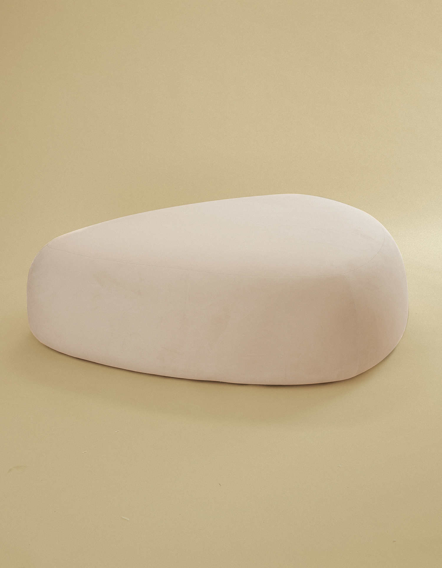 Large pebble-shaped ottoman in an off-white finish, photographed alone on a minimalist beige studio background.