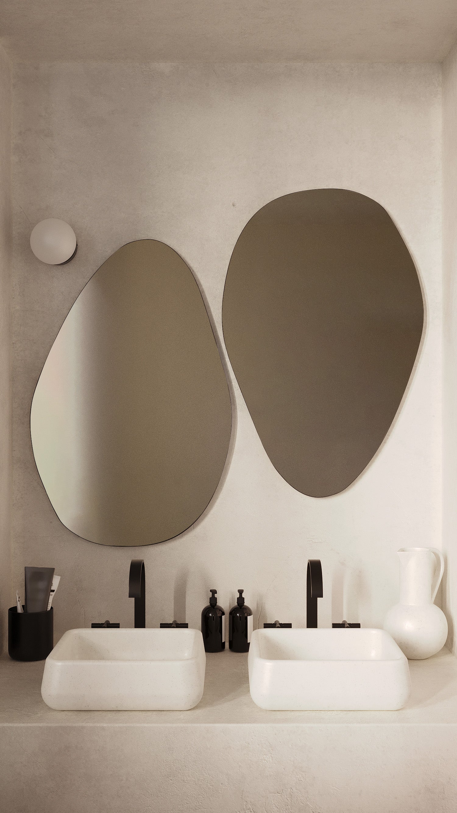 Two frameless pebble-shaped mirrors mounted above a double bathroom vanity with white vessel sinks and black faucets in a neutral-toned bathroom.