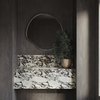 Organic-shaped stainless steel framed wall mirror mounted above a marble vanity in a modern bathroom.