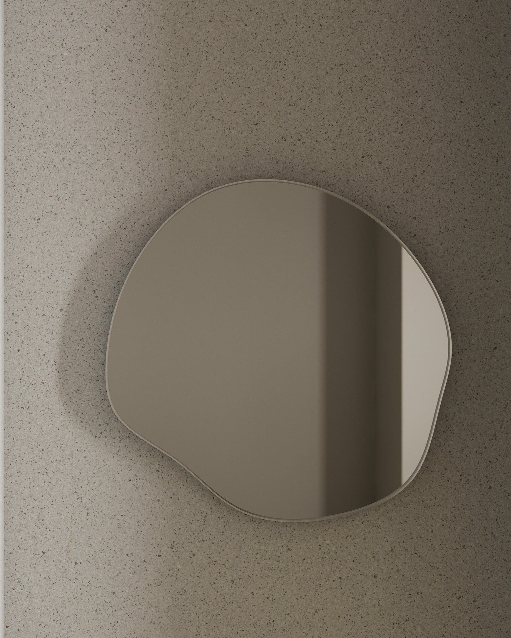 Organic-shaped wall mirror with a slim stainless steel frame mounted on a textured stone wall.