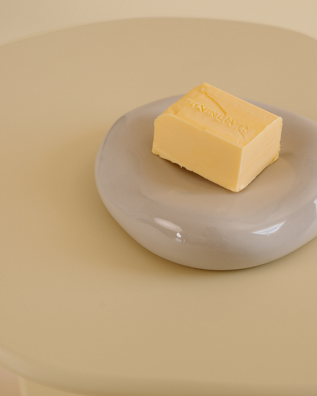 A rectangular block of butter embossed with the text “ETHNIK LIVING,” placed on a round translucent dish on top of a light yellow side table.