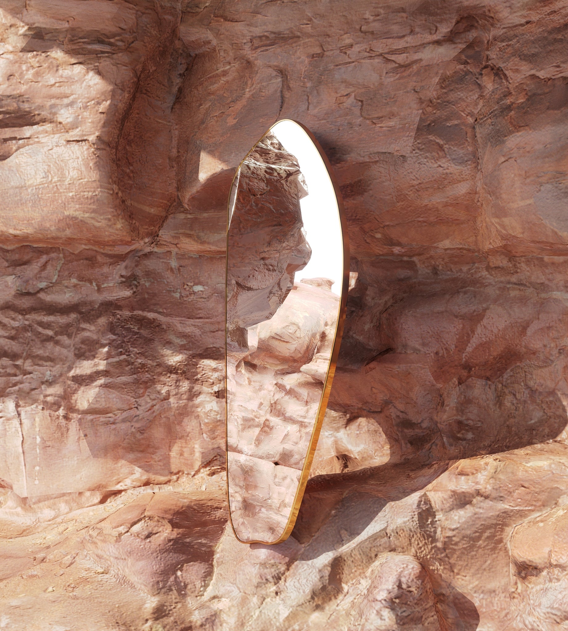 Asymmetrical brass-framed full length mirror placed against textured natural rock, reflecting the surrounding stone landscape.