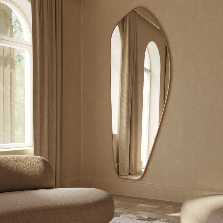 Asymmetrical brass wall mirror in a softly lit living room.