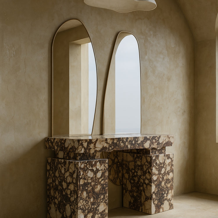 Two asymmetrical brass-framed full length mirrors mounted above a sculptural marble vanity.