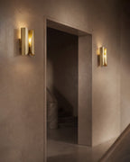 Brass wall sconces casting warm light on a textured wall beside a doorway in a minimalist interior.