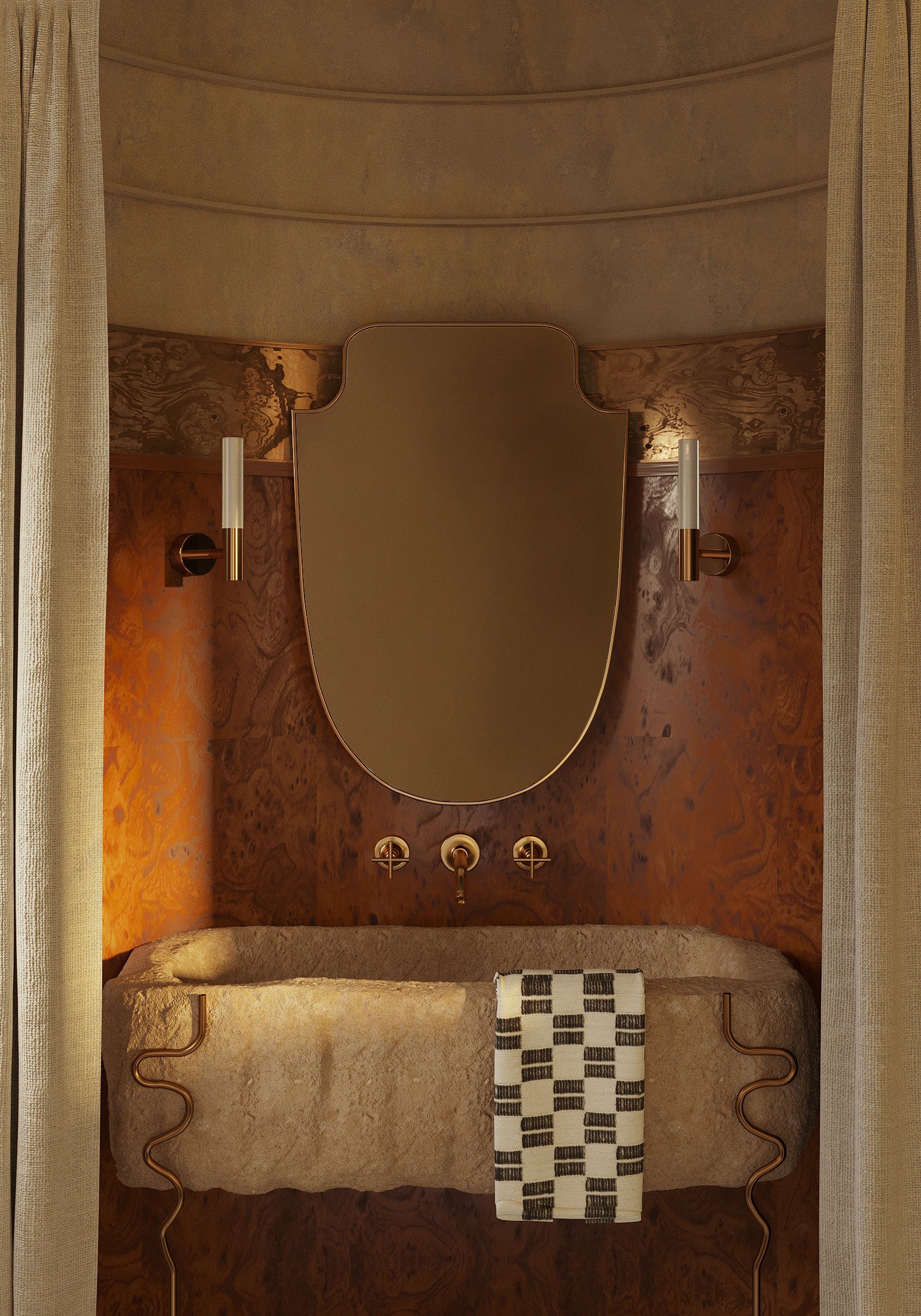 Shield-shaped wall mirror with a gold frame, mounted vertically above a bathroom vanity between two wall sconces.