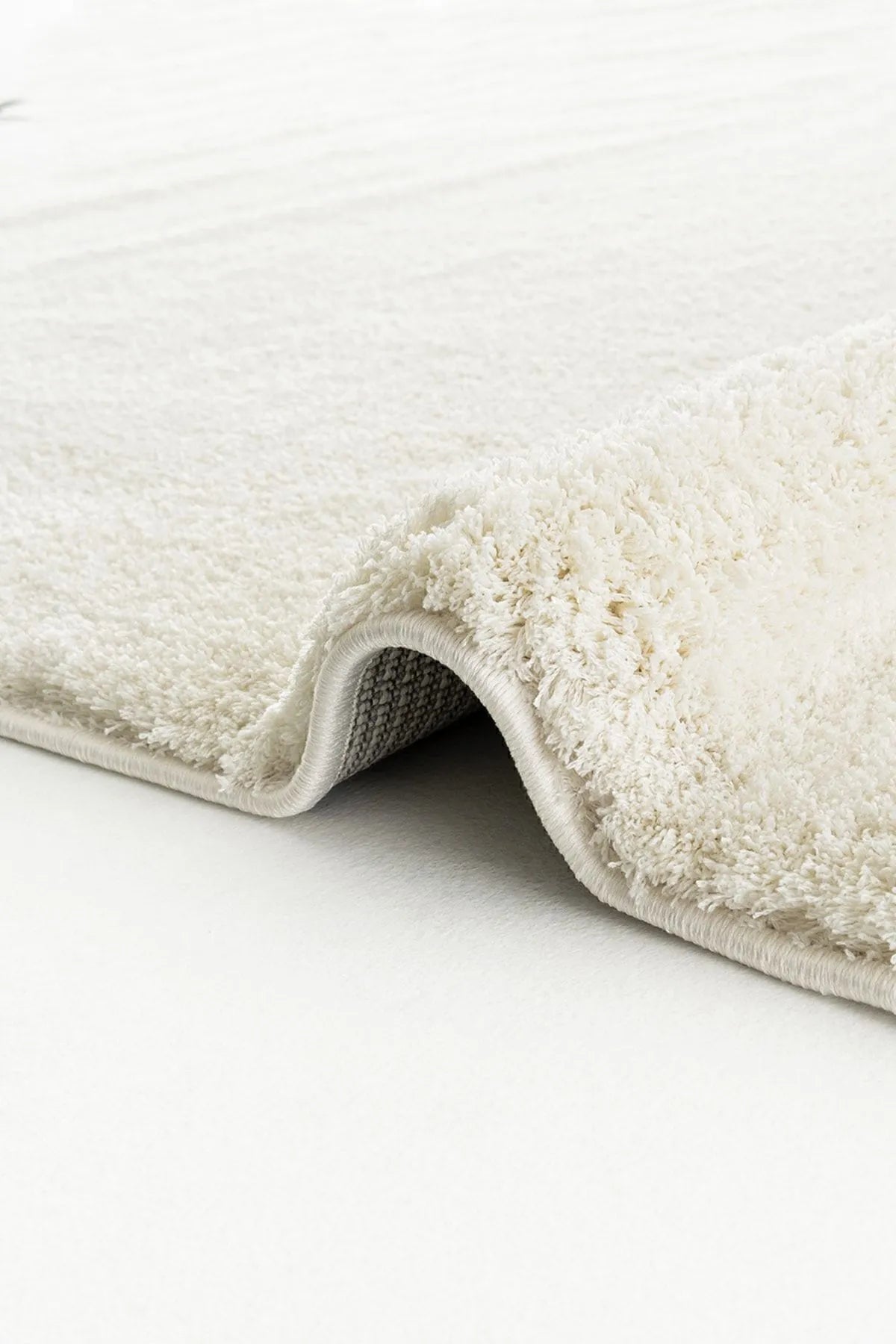 Rolled beige plush rug showing thick pile and backing.