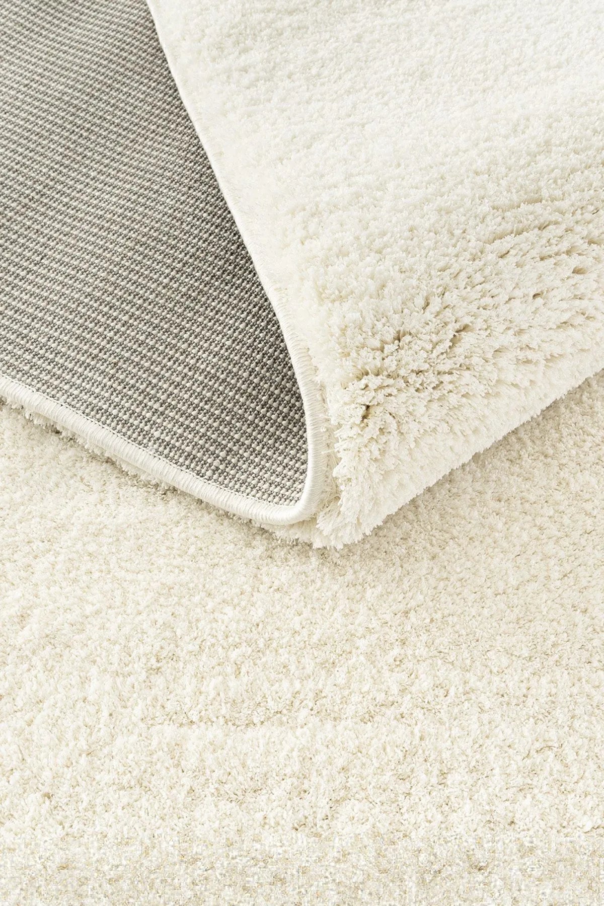 Close-up of a beige plush rug with a thick pile and woven backing.