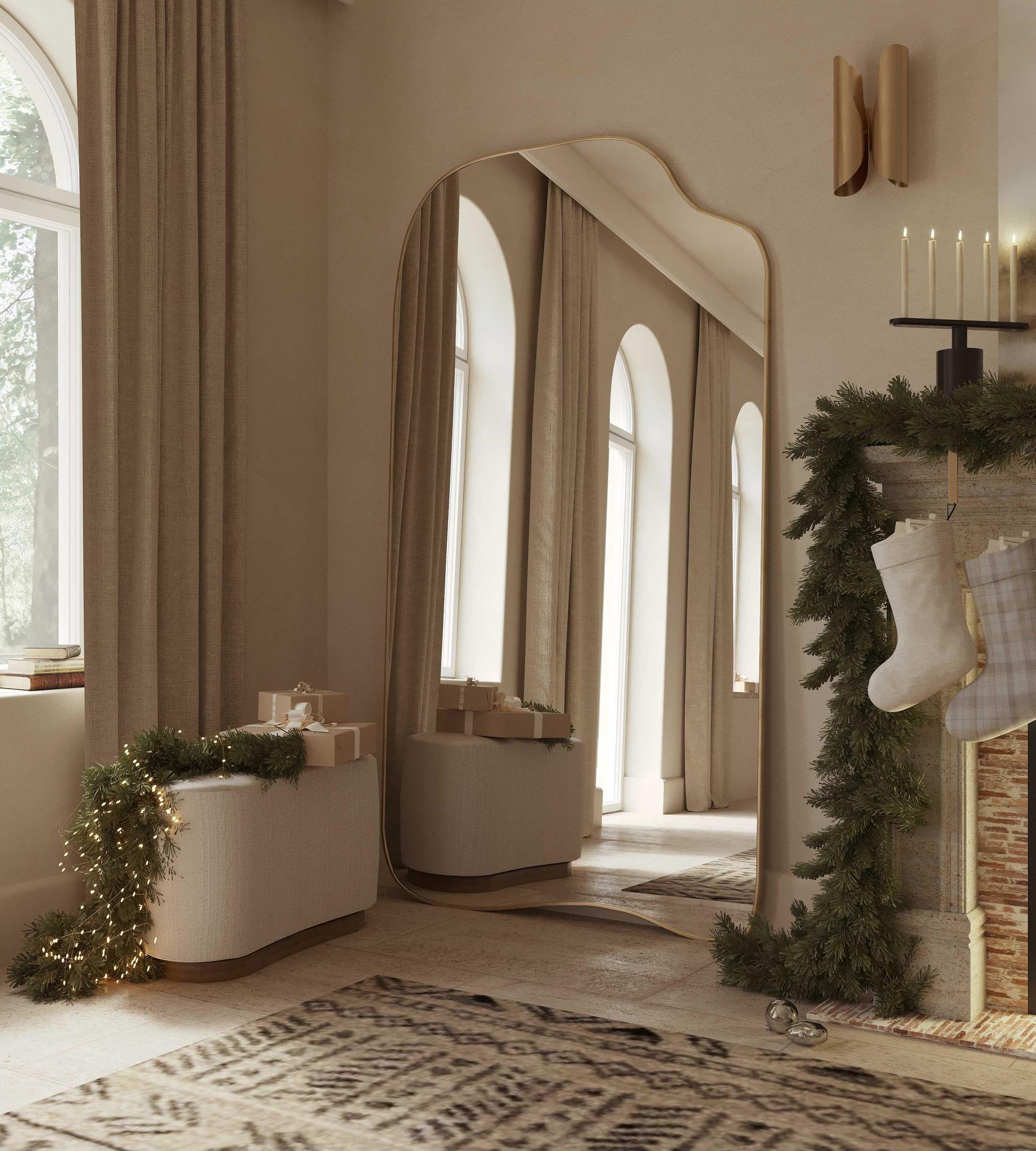 Asymmetrical full-length mirror with an organic shape and thin brass-colored frame, styled in a softly lit living space with holiday decor and arched windows.