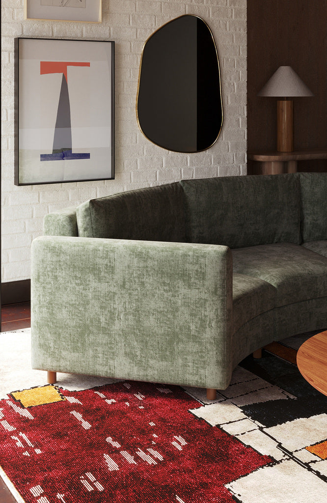 Living room with green sofa placed on an abstract red and cream patterned rug.