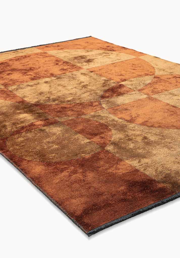 Angled view of a flat-woven rug in warm caramel, rust, and tan tones, featuring overlapping circular shapes layered over a soft checkerboard pattern with a subtly textured surface.