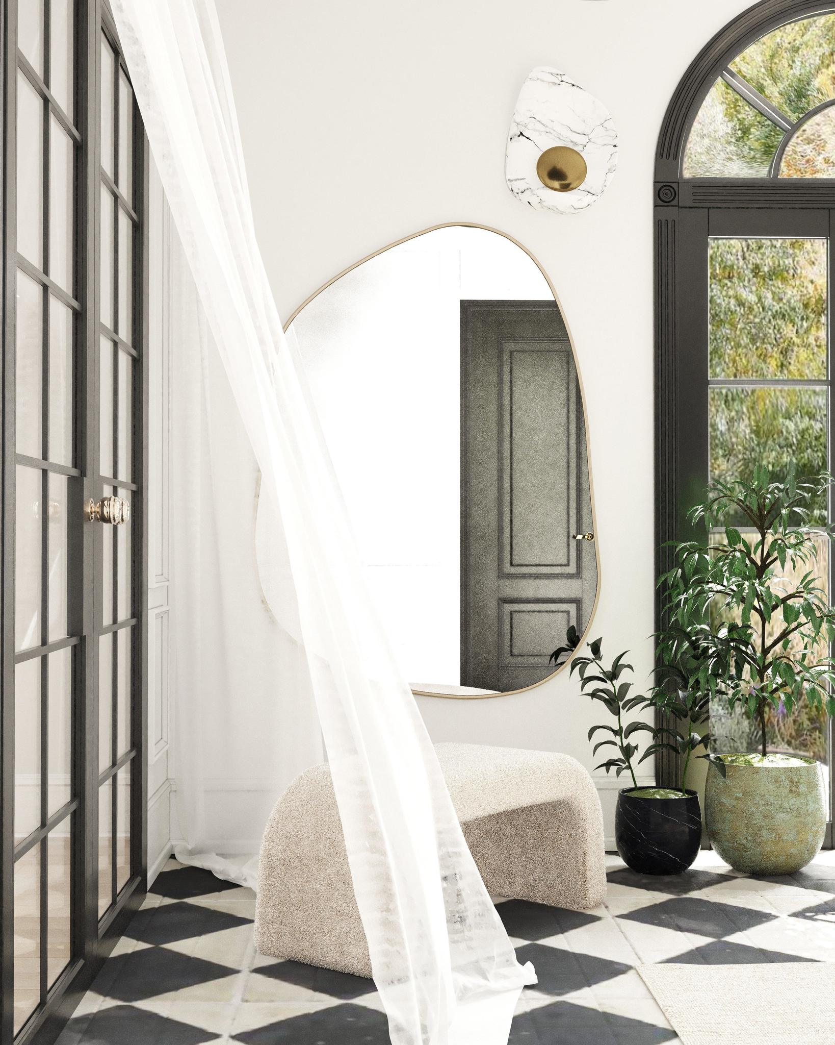 Interior space featuring an organic-shaped wall mirror, a textured bench, sheer curtain, and potted plants near arched windows.