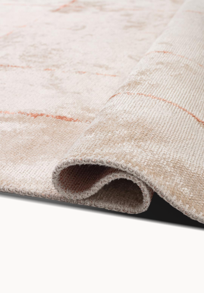 Rolled corner of a beige flat-woven rug with soft blush accents and textured weave.