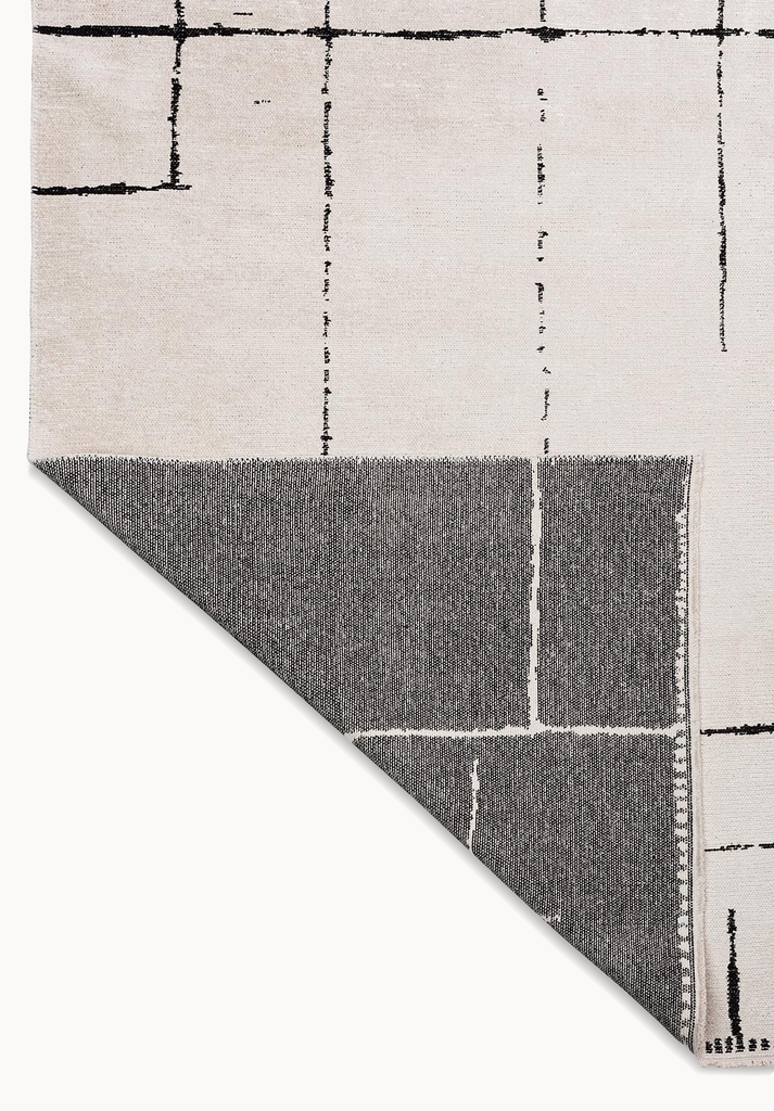 Corner detail of a beige flat-woven rug with black abstract grid lines and contrasting backing.