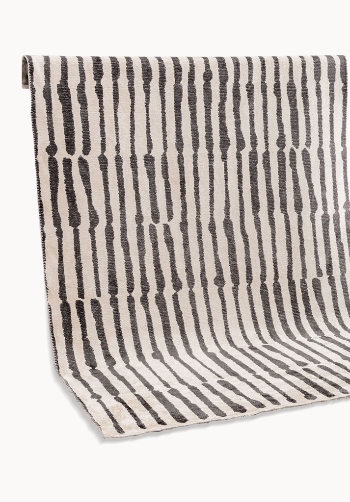 Rolled area rug with irregular black stripes on a light neutral background.