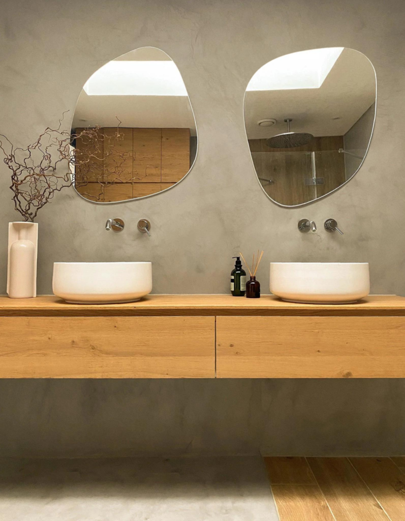 Frameless blob-shaped wall mirrors mounted above a double vanity in a modern bathroom.