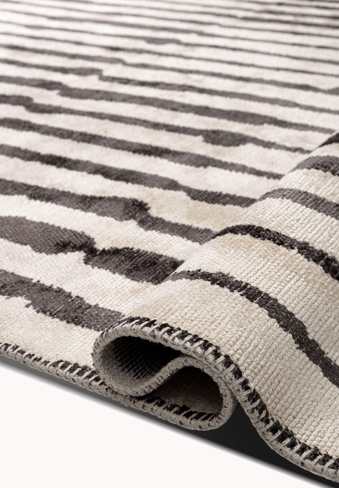 Rolled flat-woven rug with thin black stripes on a light neutral background.