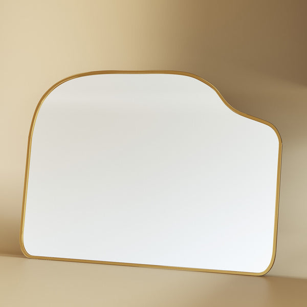 Asymmetrical brass-framed mirror displayed in a neutral studio setting with soft shadows.