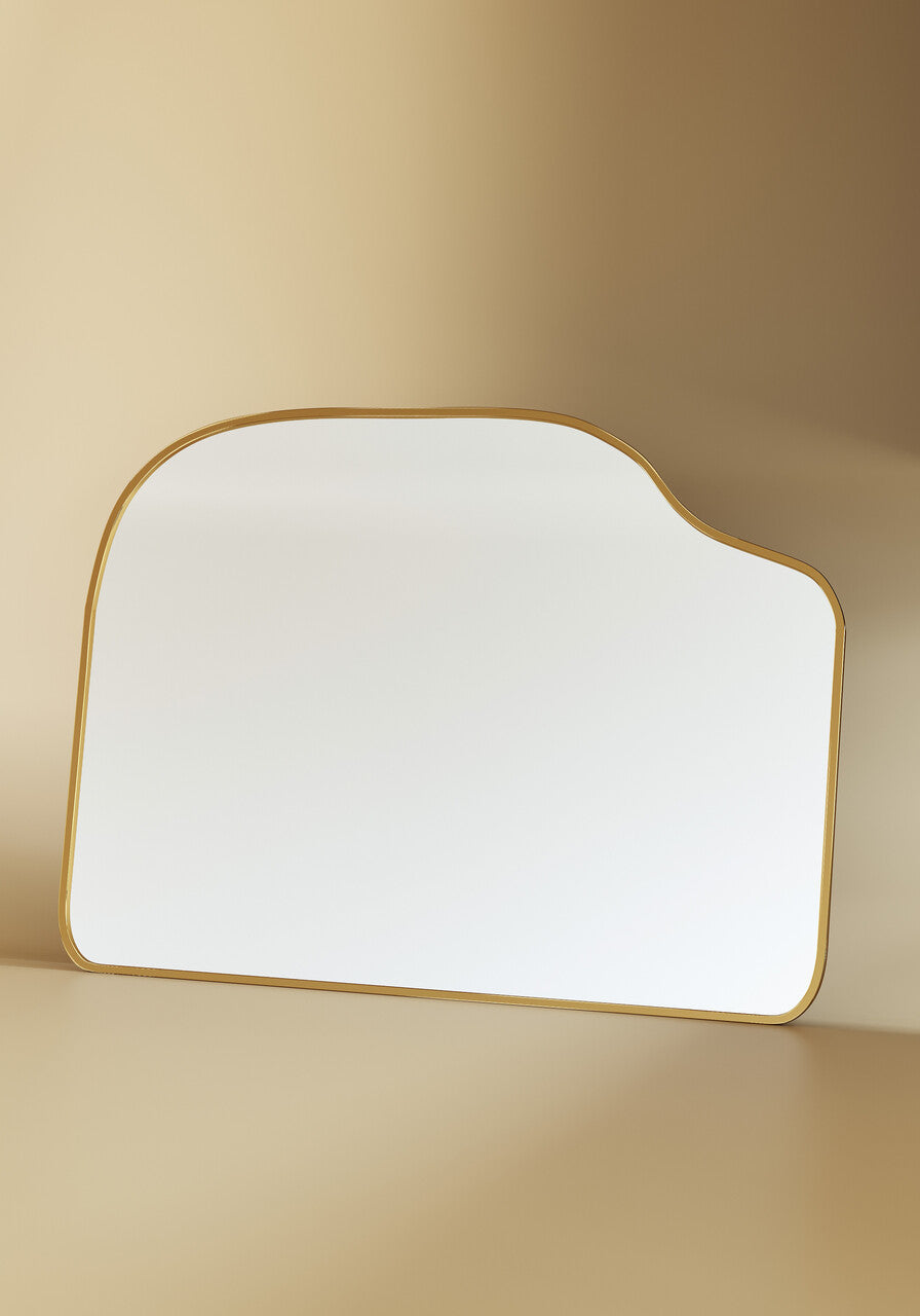 Asymmetrical brass-framed mirror displayed in a neutral studio setting with soft shadows.