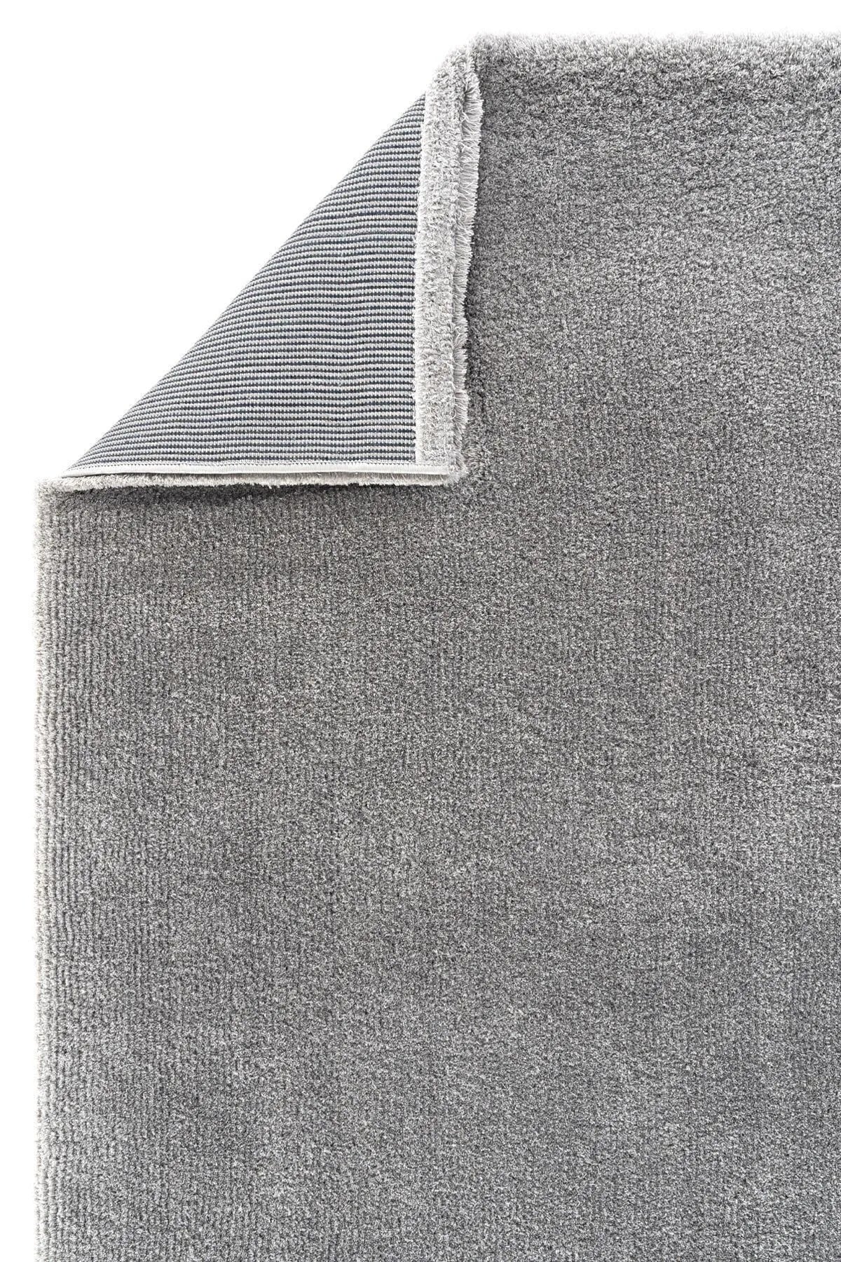 Gray plush rug with a folded corner revealing woven backing.
