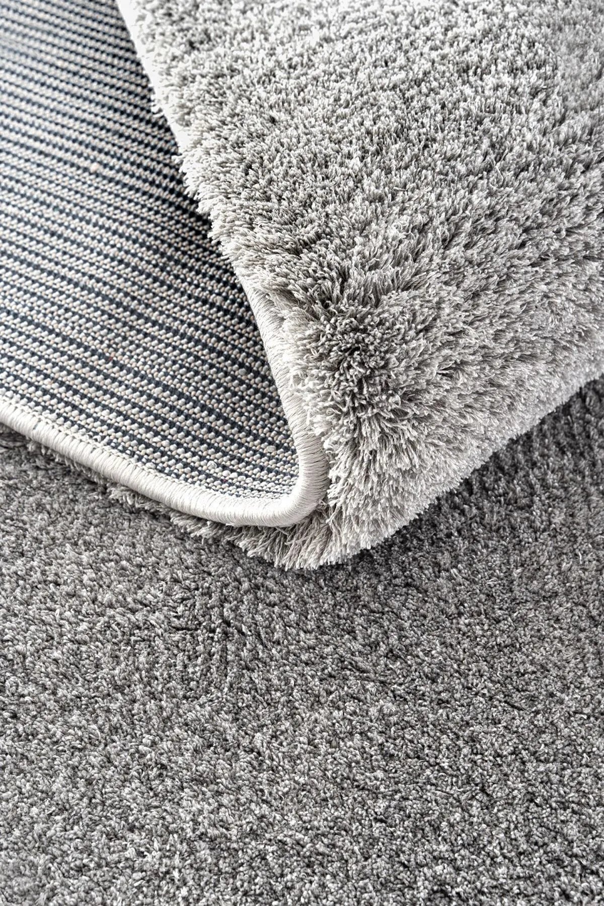 Gray plush rug with a folded corner showing textured pile and woven backing.