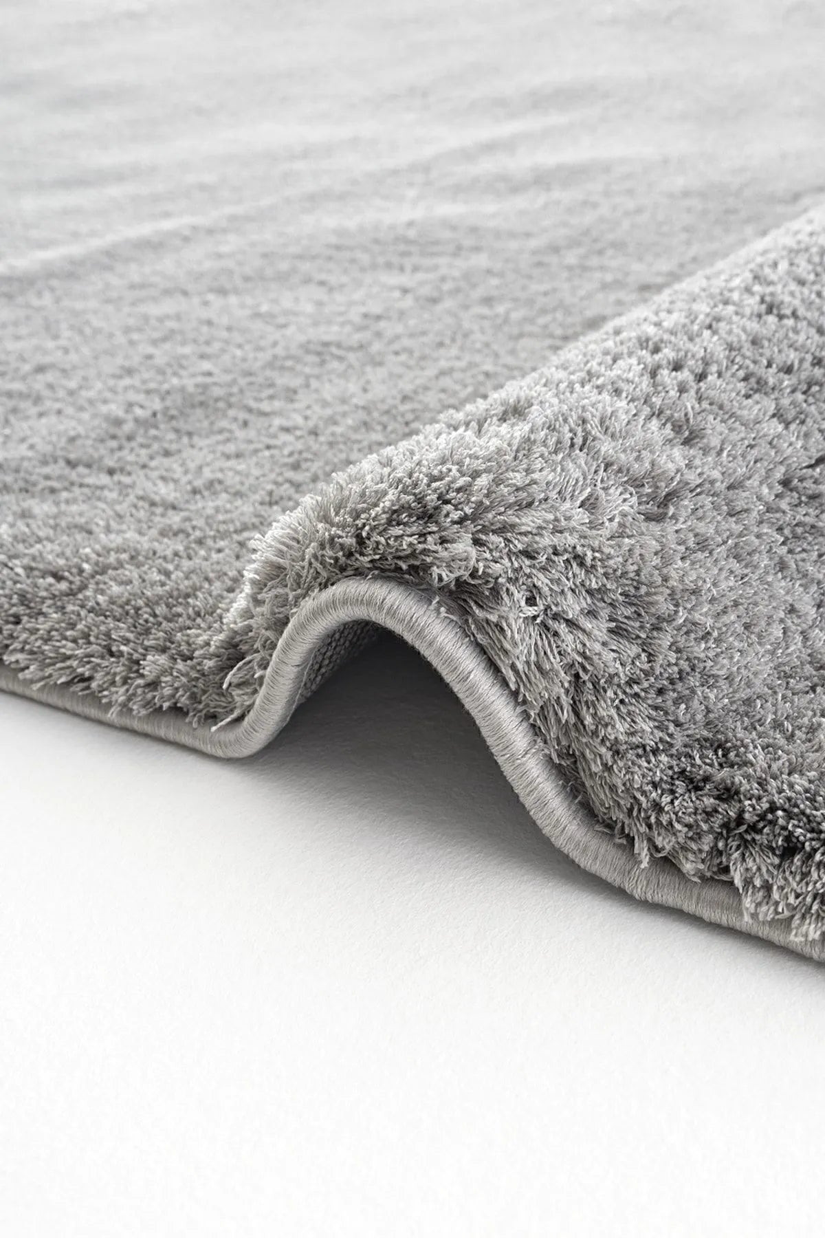 Light gray plush rug with a folded edge showing thick pile and rounded binding.