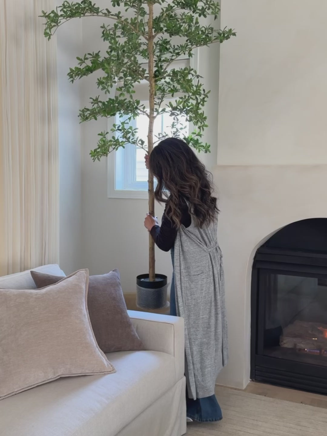A woman decorates a full-length mirror in her living room as natural daylight fills the space and reflects across the room.